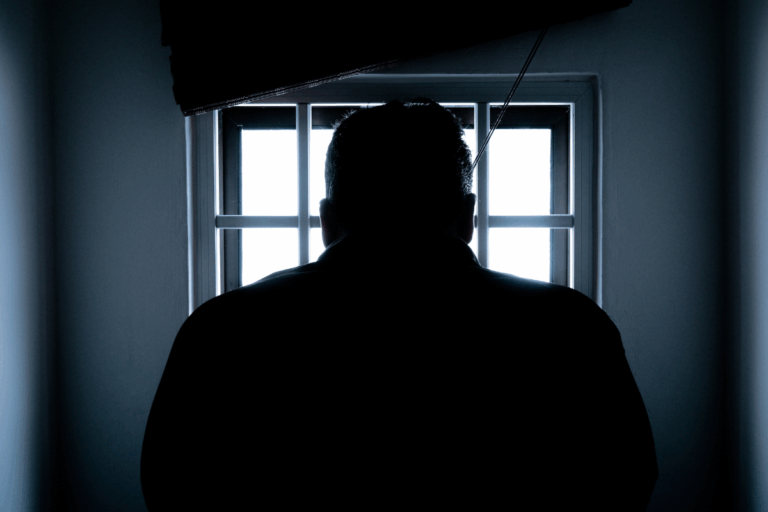 Sylwetka mężczyzny patrzącego przez kraty – ilustracja spraw karnych i obrony oskarżonych.